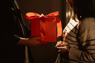 Çok sevilen bir kadına özel bir kutlama sırasında kırmızı hediye kutusu sunan adama yaklaş. Romantik sahne doğum gününü, yıldönümünü, sevgililer gününü, sevgiyi ve duygusal sürprizi simgeliyor..