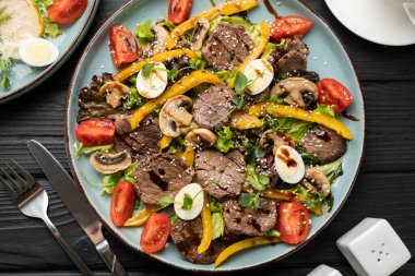 İçinde ızgara sığır eti madalyonları, canlı sarı dolma biber dilimleri, bıldırcın yumurtaları ve taze vişne domatesleri olan lezzetli sıcak salata. Beyaz tabakta servis edilen sağlıklı protein yemeği. en üstteki görünüm