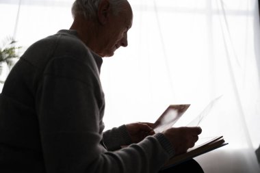 Yaşlı üzgün adamın silueti eski bir fotoğrafa benziyor. Evdeki kanepede oturan karısını kaybetmiş. Boşluğu kopyala