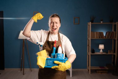 Önlüklü kızgın kadının portresi elinde kovayla temizlik malzemeleriyle oturma odasında yumruğunu sıkarak bağırıyordu. Profesyonel temizlik hizmeti kavramı