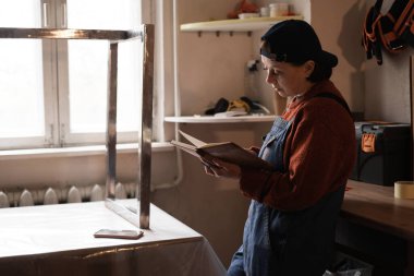 Metal bacakları masa için tamir ederken atölyedeki kadın tamircinin portresi verileri kontrol ediyor. Küçük işletme kavramı.