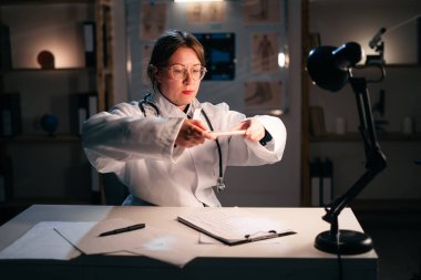 Kadın doktor telefon kullanıyor, hastanede gece vardiyası sırasında masa başında duran belgelerin fotoğrafını çekiyor. Modern cihazlar ve tıp konsepti. Boşluğu kopyala