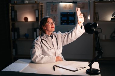 Pratisyen hekim, gece geç saatlere kadar hastane ofisinde çalışarak selfie çekiyor. Hemşire sağlık tedavisi. Boşluğu kopyala