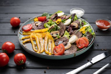 Orta pişmiş sığır eti madalyonu, ızgara biber, kiraz domatesleri ve koyu ahşap arka planda servis edilen mantarlı leziz sıcak salata. Boşluğu kopyala