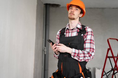 İnşaatçı, ustabaşı, alet kemeri takan bir tamirci, inşaat alanında çalışırken elinde akıllı telefon tutan bir işçi. Boşluğu kopyala