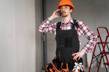 İnşaatçı, ustabaşı, alet kemeri takan tamirci inşaat alanında müşteriyle konuşurken tulum giymiş. Boşluğu kopyala