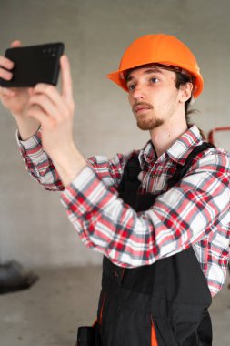 İnşaatçı, ustabaşı, tamirci, alet kemeri takan ve inşaat alanında iş tulumu giyen biri akıllı telefondan fotoğraf çekiyor. Boşluğu kopyala