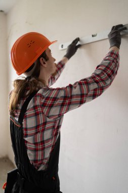 Müteahhit, tamirci, üniformalı müteahhit balon ruh seviyesini kullanarak duvarı ölçüyor. Ev yenileme ve inşaat konsepti. Boşluğu kopyala