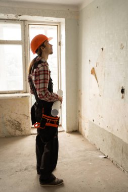 Çizimleri olan bir tamirci yenileme ve yenilemeden önce eski bir evdeki döşeme duvarına bakar. Boşluğu kopyala