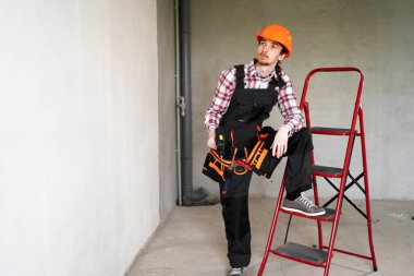 Düşünceli erkek işçi, tamirci ya da tamirci tamir ya da onarıma hazır, tulum giyiyor ve koruyucu başlık takıyor, inşaat alanında çalışıyor.