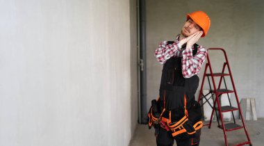 Erkek işçi, inşaatçı veya tamirci uyku jesti yapmaya hazır, tulum, alet kemeri ve koruyucu başlık giyiyor, inşaat alanında çalışıyor. Boşluğu kopyala