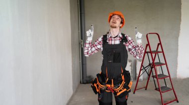 Erkek işçi, inşaatçı ya da tamirci fotokopi alanını işaret eden, tulum giyen, alet kemeri takan ve inşaat alanında çalışan tamirci diyor. Pankart