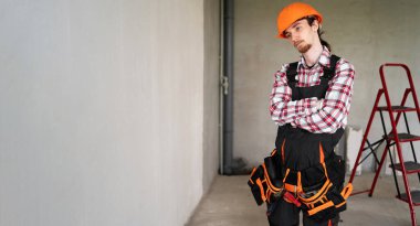 İnşaat alanında tamirat için hazır, miğfer ve alet kemeri takan yorgun, üzgün erkek işçi, tamirci veya tamirci. Pankart. Boşluğu kopyala