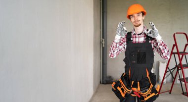 Erkek işçi, miğfer ve alet kemeri takan tamirci veya tamirci, inşaat ve onarım için hazır olduğunu söylüyor. Pankart