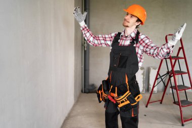 İnşaat alanında tamirat ya da tamirat için hazır, miğfer ve alet kemeri takan mutlu, duygusal işçi, inşaatçı ya da tamirci. Boşluğu kopyala