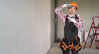 Şen duygusal işçi, miğfer ve alet kemeri takan tamirci ya da tamirci inşaat alanında büyük kutu jestlerini göstermeye hazır. Pankart. Boşluğu kopyala