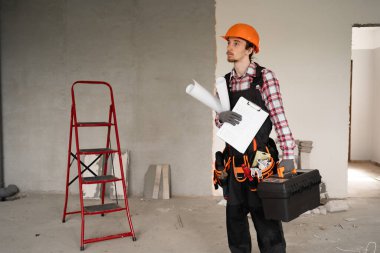 Ev onarımı konsepti. Kask takan genç işçi, tamir için alet çantası taşıyor. Elinde de yenileme için gerekli aletler var. Boşluğu kopyala