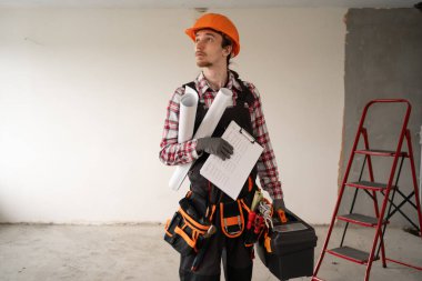 Ev onarımı konsepti. Kask takan genç işçi, tamir için alet çantası taşıyor. Elinde de yenileme için gerekli aletler var. Boşluğu kopyala