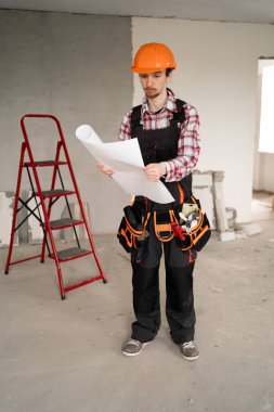 Erkek inşaat işçisi inşaat alanının planlarını okurken başlık takıyor. Boşluğu kopyala