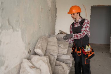 İnşaat enkazı toplayan kasklı genç bir inşaatçı. Ev yenileme ve onarım konsepti. Boşluğu kopyala