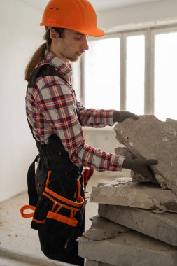 İnşaat enkazı toplayan kasklı genç bir inşaatçı. Ev yenileme ve onarım konsepti. Boşluğu kopyala