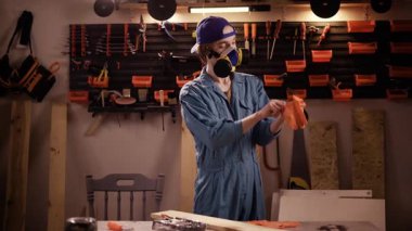 Atölyesindeki marangoz, hayati önem taşıyan tahta mobilya restorasyon projesine başlamadan önce koruyucu eldivenler ve solunum cihazını dikkatlice takıyor.