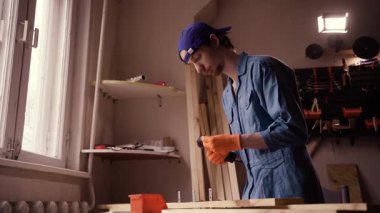 Marangozluk atölyesinde çalışan üniformalı genç bir marangoz kereste kuyusu açıyor. Boşluğu kopyala