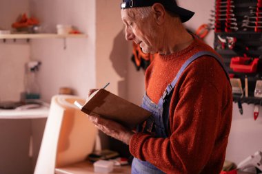 Yaşlı erkek tamirci, atölyede müşteri ile telefon görüşmesi yapıyor. yan görünüm