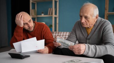 Mutsuz yetişkin bir adam ve yaşlı babası, faturaların masraflarını hesaplayarak, parasız olduklarını vurguladılar. Boşluğu kopyala