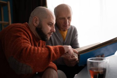 Sevgi dolu yetişkin oğlu ve yaşlı babası evde aile fotoğraflarına bakıyor. Babalar günü. Boşluğu kopyala