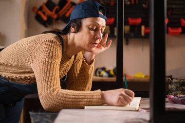 Küçük işletme sahibi, bir metal atölyesinde deftere bakım notları yazıyor. Boşluğu kopyala