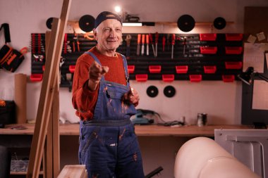 Olgun marangoz kamerayı işaret ederek atölyedeki mobilya yenileme projesi için seni seçtiğimi gösteriyor. El yapımı, küçük işletme, DIY, seçim konsepti.