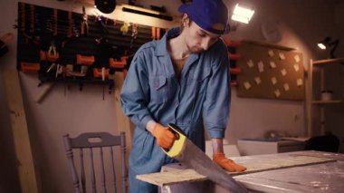Eldiven ustası, marangozluk atölyesinde geleneksel bir testereyle sert bir OSB tahtasını titizlikle kesti..