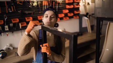 Kadın tamirci atölyesinde metal işçiliği yapıyormuş. Duvarda düzenlenmiş aletler. Boşluğu kopyala