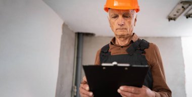 Kıdemli mimar, inşaat mühendisi ya da müteahhit miğferli ve panosu olan yaşlı bir adam, bina teftişi. İnşaat alanında çalışan bir inşaat işçisi. meslek, inşaat ve onarım kavramı.