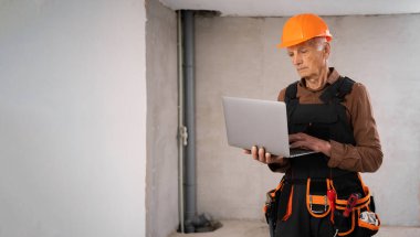 Çalışma alanında dizüstü bilgisayar kullanan bir mimar. İnşaat mühendisi yaşlı bir adam internetten malzeme alıyor. Küçük işletmelerde inşaat işçisi. Müteahhit ya da müteahhit. kopyalama alanı. Pankart