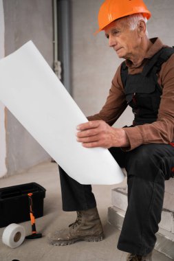 Miğfer ve tulum giyen üst düzey müteahhit inşaat sektöründe uzmanlık sergileyen kağıt taslağı okuyor. meslek, inşaat ve onarım konsepti. Boşluğu kopyala