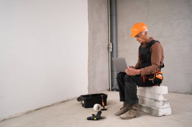 İnşaatçı ya da tamirci miğferli üst düzey bir adam yenileme işlemi sırasında dizüstü bilgisayarla inşaat alanında sipariş veriyor. meslek, inşaat ve onarım konsepti. Boşluğu kopyala