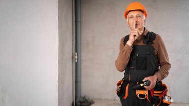 Güvenlik miğferi kaplı üst düzey tamirci ya da tamirci tadilat sırasında inşaat alanında gizli bir jest yapmanı söylüyor. meslek, inşaat ve onarım kavramı.