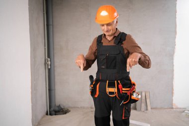 Güvenlik miğferi takmış tamirci ya da tamirci yenileme işlemi sırasında inşaat alanındaki alet kemeri reklam aletlerini işaret ediyor. Daire onarımı ve yenileme konsepti.