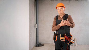 Minnettar İnşaatçı ya da güvenlik kaskı takmış tamirci yenileme işlemi sırasında inşaat alanında sevgi dolu kalp hareketi yapan yaşlı bir adam. Daire onarımı ve yenileme konsepti.