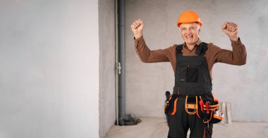 İnşaatçı ya da tamirci, güvenlik kasklı kıdemli adam yenileme işlemi sırasında şantiyede zafer kutluyor. meslek, inşaat ve onarım kavramı.