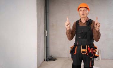 İnşaat alanında kasklı bir inşaat işçisi ya da kıdemli tamirci alet kutusunun yanında oturuyor ve işaret parmağıyla bir reklam alanına işaret ediyor. meslek, inşaat ve onarım kavramı.