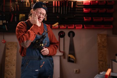 Tamir atölyesinde çalışırken diş ağrısı çeken tulumlu ve gözlüklü bir kadın tamirci. Boşluğu kopyala