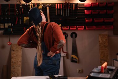 Tulumlu ve gözlüklü kadın tamirci tamirhanede çalışırken sırtı ağrıyormuş. Boşluğu kopyala