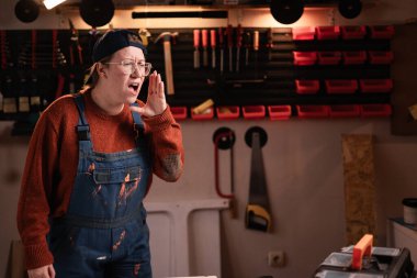 Tulumlu ve gözlüklü kadın tamirci tamirhanede çalışırken satışlarla ilgili sıcak haberleri paylaşırken çığlık atıyor. Boşluğu kopyala