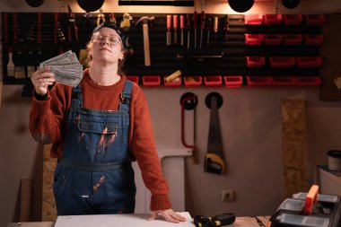 Tulumlu ve gözlüklü kadın tamirci atölyede çalışırken atölyede nakit parayla dinleniyor. Boşluğu kopyala