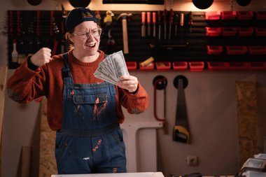 Tulumlu ve gözlüklü başarılı kadın tamirci atölyede çalışırken atölyede piyango kazanmasını kutluyor. Boşluğu kopyala