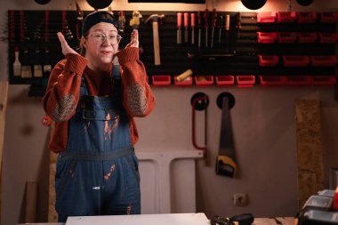 Tulumlu ve gözlüklü kadın tamirci atölyede çalışırken atölyede gülen yüz ifadesini gösteriyor. Boşluğu kopyala