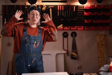 Tulumlu ve gözlüklü kadın tamirci atölyede çalışırken atölyede gülen yüz ifadesini gösteriyor. Boşluğu kopyala